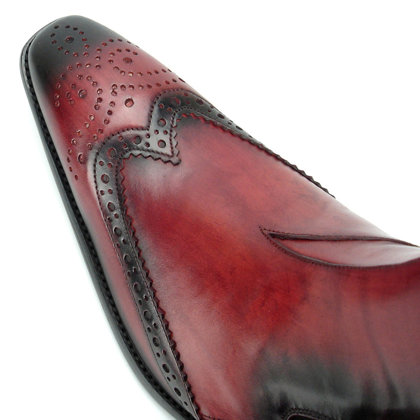 A handcrafted burgundy leather Chelsea boot with black wingtip brogue detailing, elastic side panels, and a low heel—shown on a white background—FI-8708 Wing Tip Boot Encore by Fiesso exemplifies men’s fashion boots from the brand.