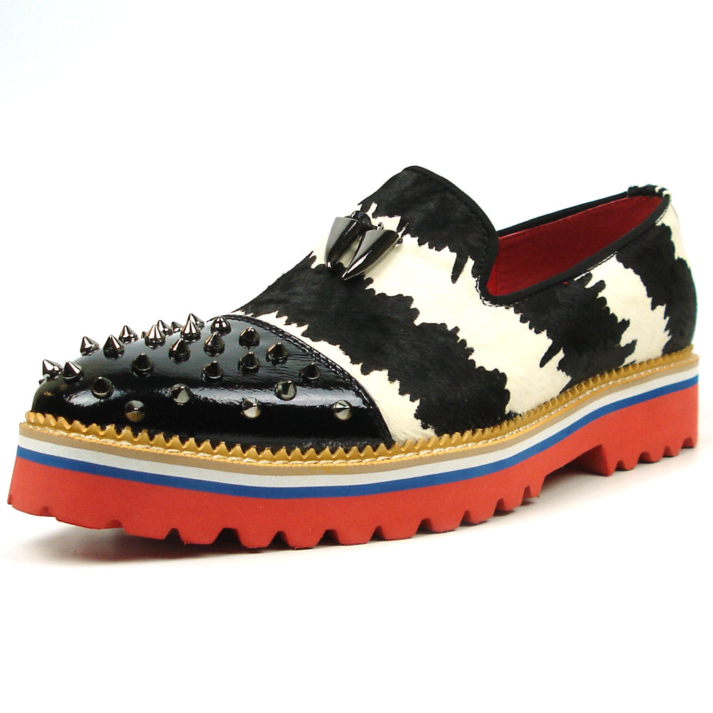 The FI-7455 Black White Cap Toe Spikes Slip On with Tassel by Fiesso features handcrafted leather, a red sole, blue trim, metal studs on the toe, and bold triangular metal accents—perfect for standout men’s fashion.