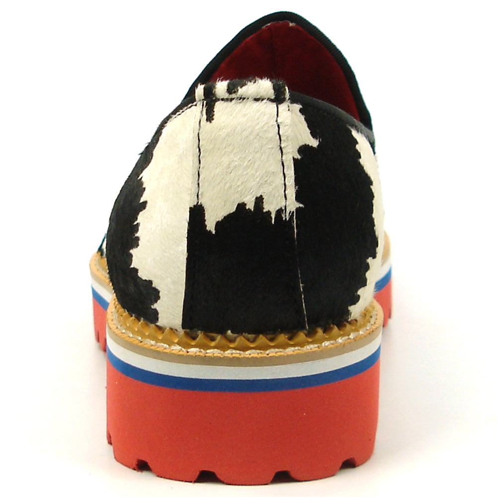 The FI-7455 Black White Cap Toe Spikes Slip On with Tassel by Fiesso features handcrafted leather, a red sole, blue trim, metal studs on the toe, and bold triangular metal accents—perfect for standout men’s fashion.