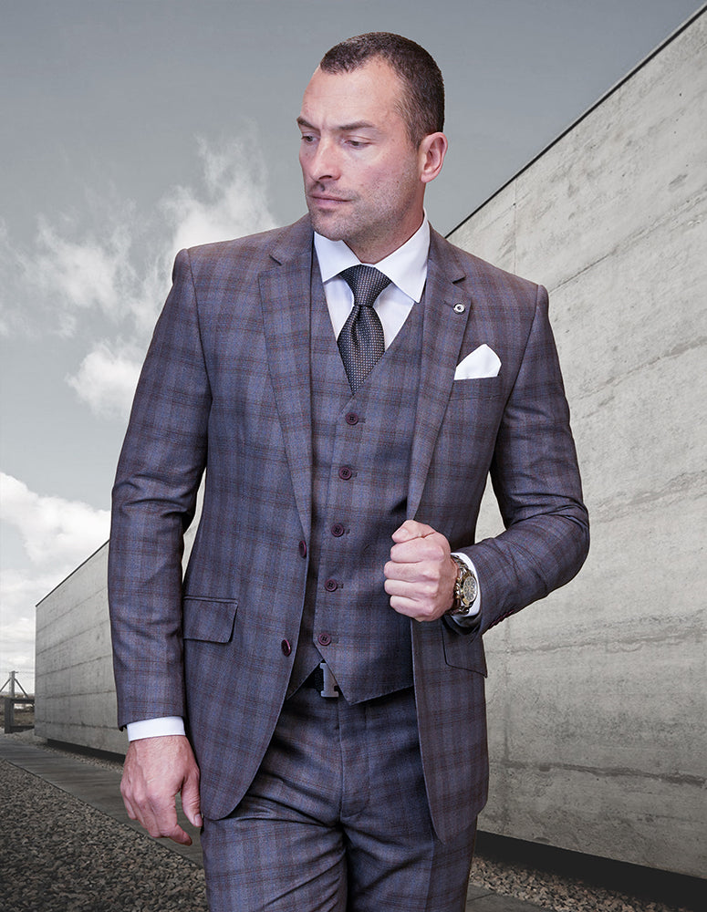A man in the STATEMENT CLOTHING | GALELI-TAUPE brown plaid Italian wool suit by Statement Clothing, styled with a white shirt and dark tie, stands outdoors against a sleek concrete wall.