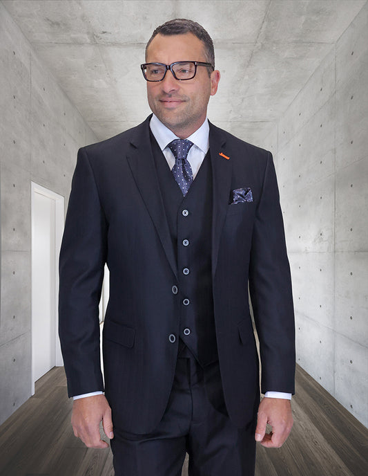 A man wears the STATEMENT CLOTHING | GARDA-BLACK Italian wool suit with a double-breasted vest and modern fit pants, standing in a hallway with concrete walls and wood flooring, looking slightly to the side.