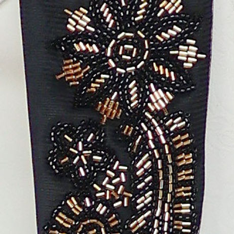 A man in a Manzini Giorgio 3PC slim fit tan tuxedo with a floral pattern, black bead lapel by Insomnia, stands against a textured stone wall, wearing a white shirt and bow tie.