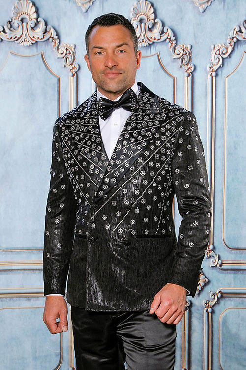 A person in the Insomnia MANZINI GQ-400 Slim Fit Rhinestone Double Breasted Black Tuxedo stands against an ornate blue background, the satin catching light elegantly.