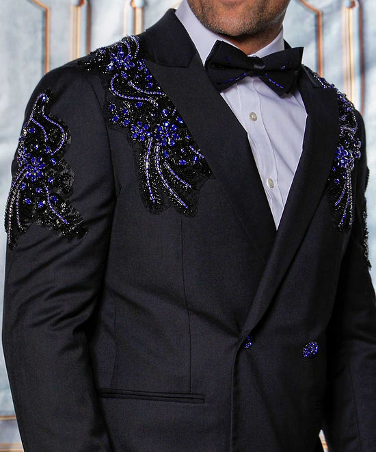 A man wears the Insomnia MANZINI GQ300 slim fit double-breasted black/royal tuxedo suit with rhinestone pattern, standing in front of an ornate, light-colored backdrop.