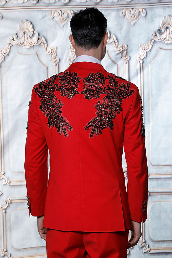 A man wears the Manzini GQ300 2-piece slim fit rhinestone pattern double-breast red tuxedo suit, standing before an ornate backdrop.