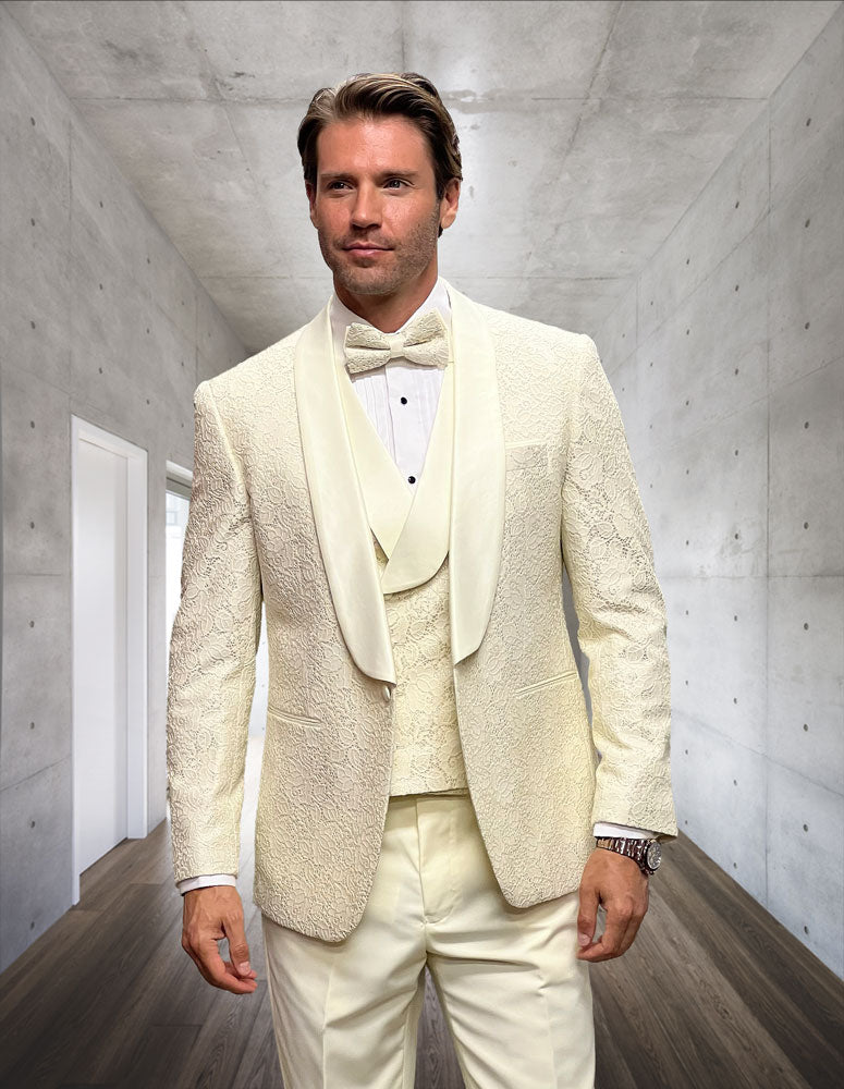 A man wearing the STATEMENT CLOTHING | GRAMMY-OFFWHITE tuxedo by Statement Clothing stands in a modern hallway with concrete walls and wooden floors.