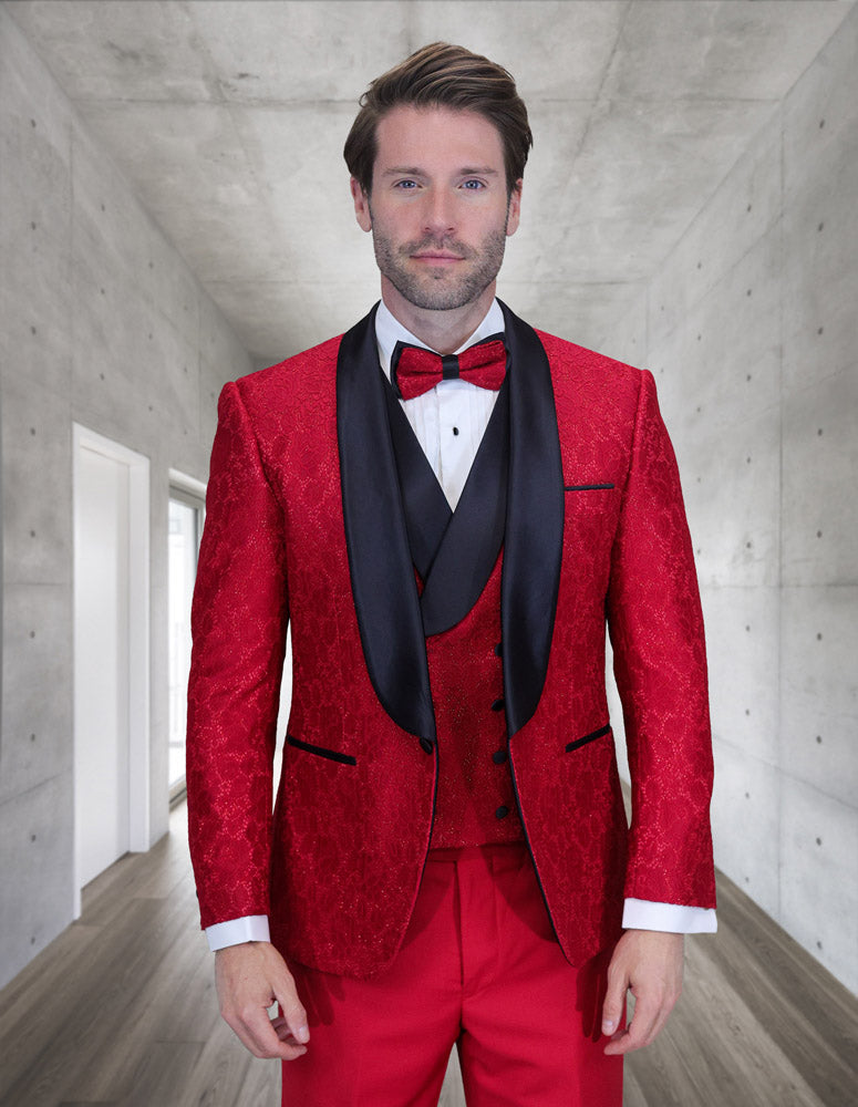 A man stands in a modern hallway wearing the STATEMENT CLOTHING | GRAMMY-RED tuxedo from Statement Clothing, featuring black lapels, a matching red bow tie, white dress shirt, and a stylish double-breasted vest.