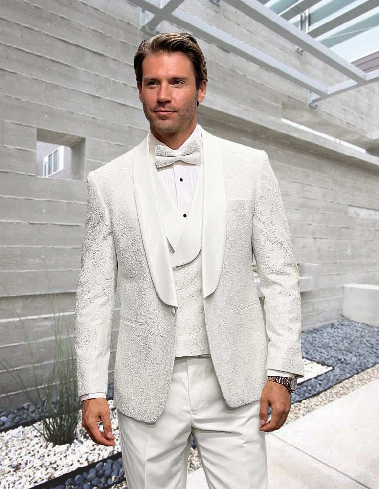 A man wears the STATEMENT CLOTHING | GRAMMY-WHITE tuxedo by Statement Clothing, featuring a matching vest and bow tie, as he stands in a modern outdoor space with concrete walls and landscaping.
