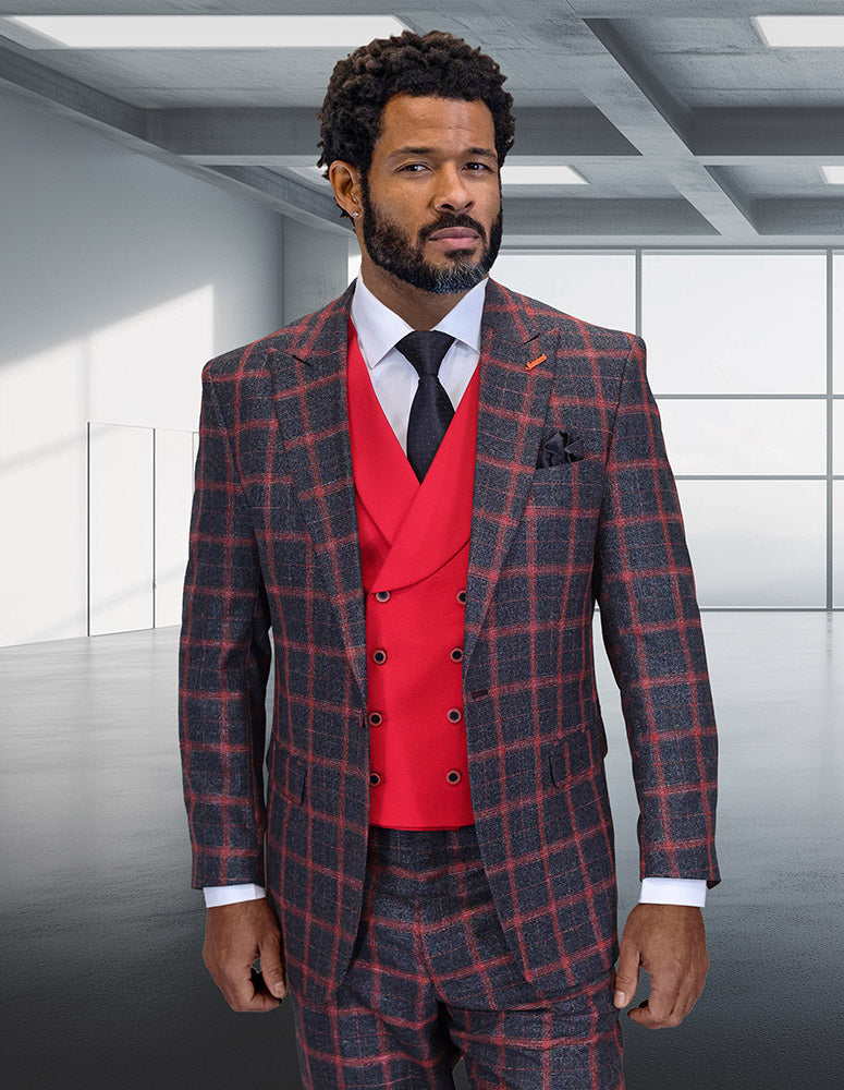 A bearded man stands in a modern, empty room, dressed in the STATEMENT CLOTHING | HARTFORD-BLACK-RED Italian Wool Suit by Statement Clothing, featuring a gray and red plaid pattern with a red double-breasted vest over a white shirt and black tie.