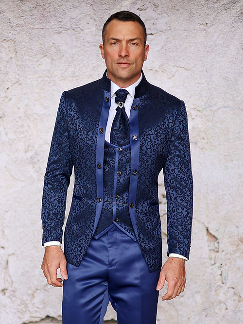 A man stands against a textured light wall wearing the MANZINI HAVANA 3-Piece Slim Fit Shiny Satin Pattern Banded Collar Sapphire Suit by Insomnia, featuring a fitted dark blue ensemble with a subtle floral pattern, matching vest, and tie. Dry clean only to maintain its pristine condition.