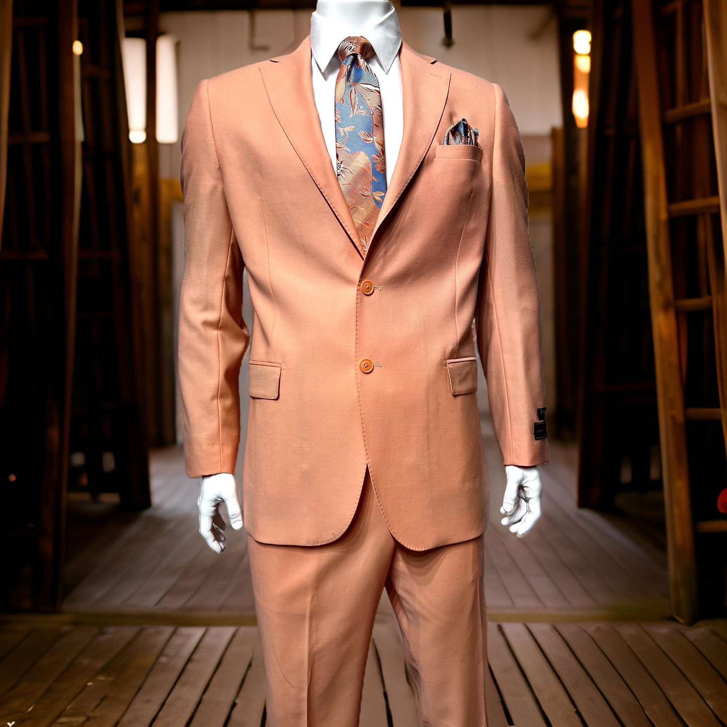 A mannequin dressed in the Tiglio Luxe Dolcetto Modern Fit Peach Suit TL4013, paired with a patterned tie, stands on a wooden floor among ladders and lights, highlighting the elegance of Italian fabrics in men's clothing.