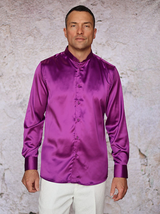 A man poses by a light textured wall in the Manzini MANZINI IN-101 Regular Collar Solid Color Satin Shirt in purple—an elegant, shiny long-sleeve shirt paired with white pants, perfect for formal occasions.