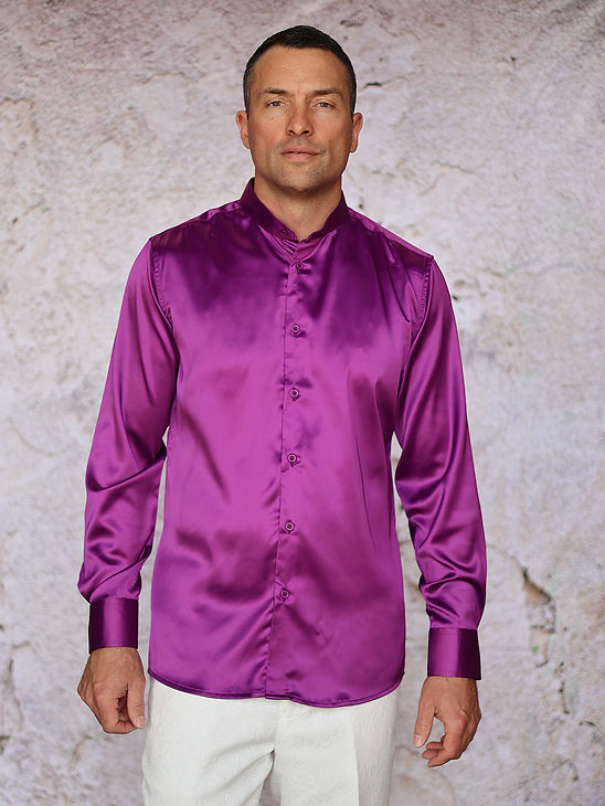 A man stands against a textured light wall, wearing the Manzini INR-102 Banded Collar Solid Color Satin Shirt in purple by Manzini with long sleeves and white pants.