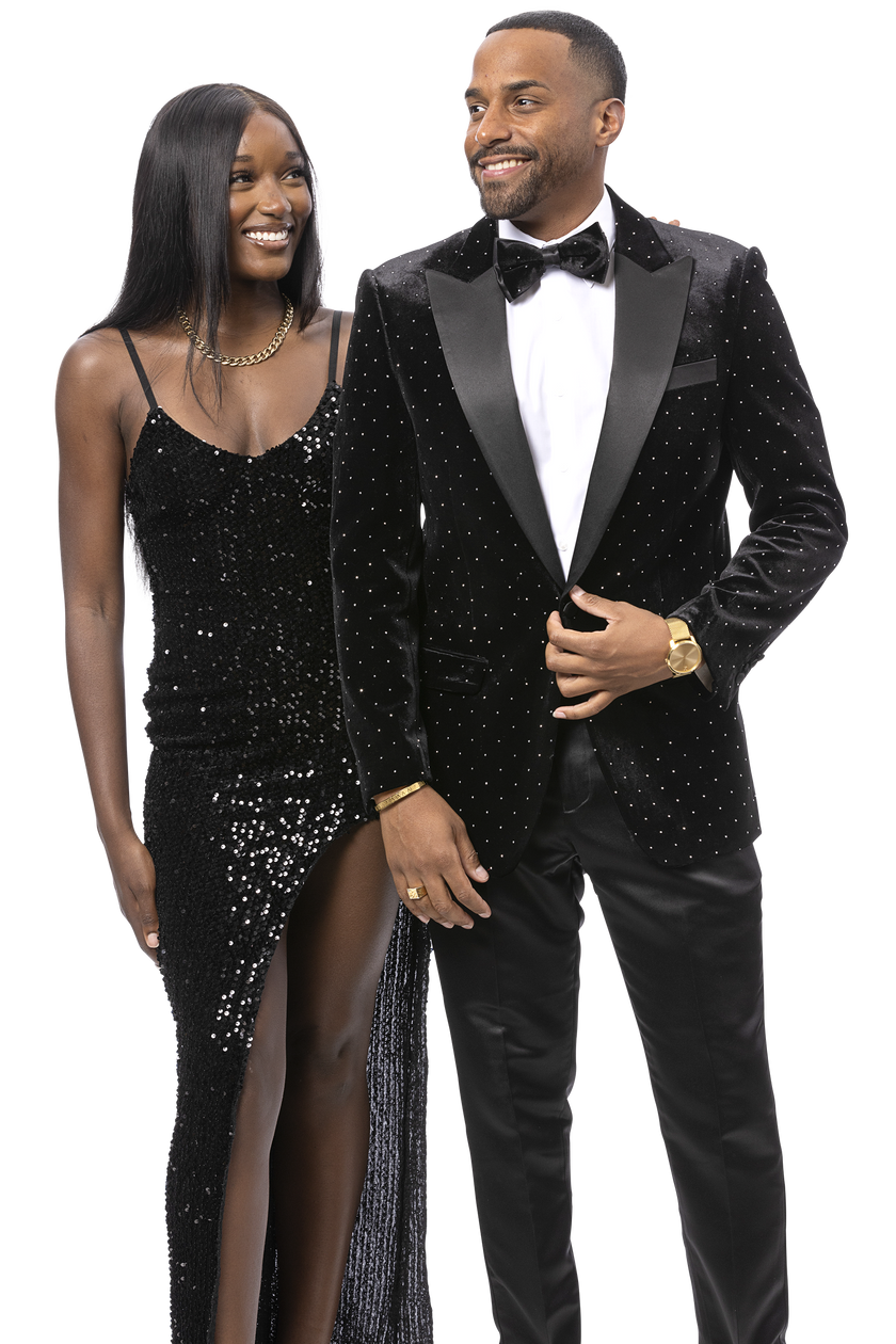 A woman in a black sequin dress with a thigh-high slit stands beside a man wearing the EJ SAMUEL Black Blazer J195. Both are smiling and looking at each other.