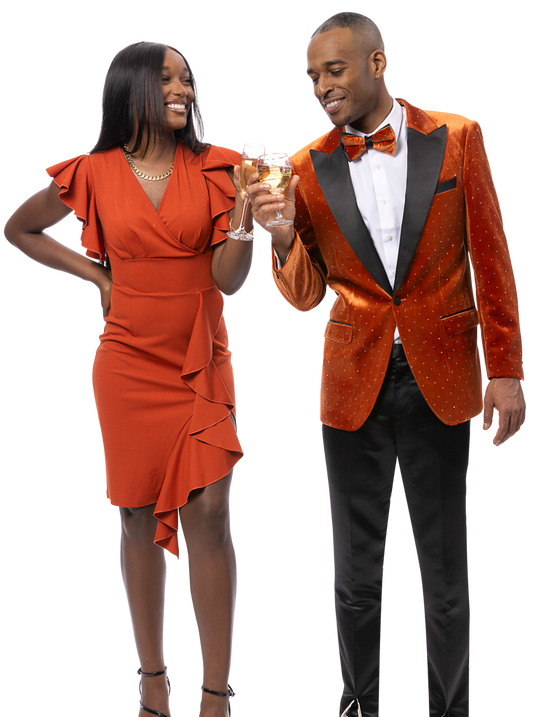 A woman in a ruffled orange dress and a man in the EJ SAMUEL Rust Blazer J197 clink glasses and smile.