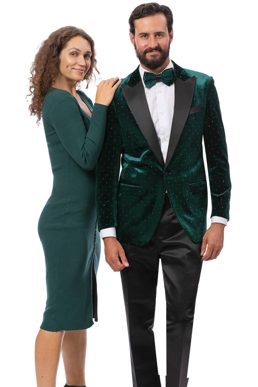 A woman in a fitted green dress stands next to a man in the EJ SAMUEL Green Blazer J198, featuring velvet fabric, satin lapel, white shirt, and black pants; both face the camera and smile.