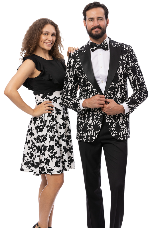 A woman in a black top and floral skirt stands next to a man wearing the EJ SAMUEL EJ Samuel Blk/White Blazer J203, paired with a crisp white shirt and matching bowtie.