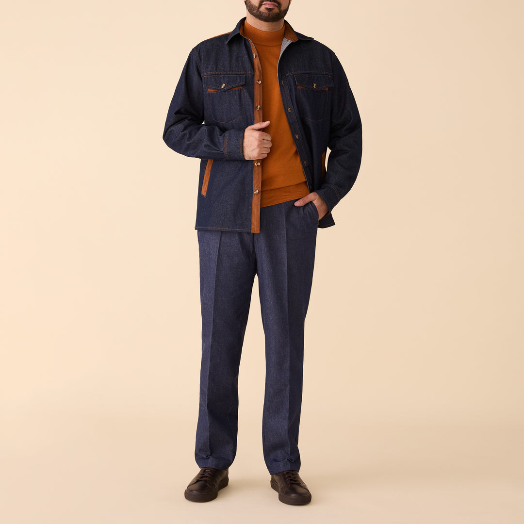A man stands against a beige background wearing the Inserch Denim Shirt Jacket with Suede Trim 2pc Set (JS005-P005-00195 Indigo) by Inserch, styled with an orange sweater and dark brown shoes.