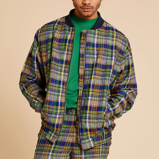 A person wearing a green shirt and the Inserch Linen Madras Bomber Jacket JS259-66 Multi, a colorful zip-up by Inserch with a dark ribbed collar, shown from the chest up against a beige background.