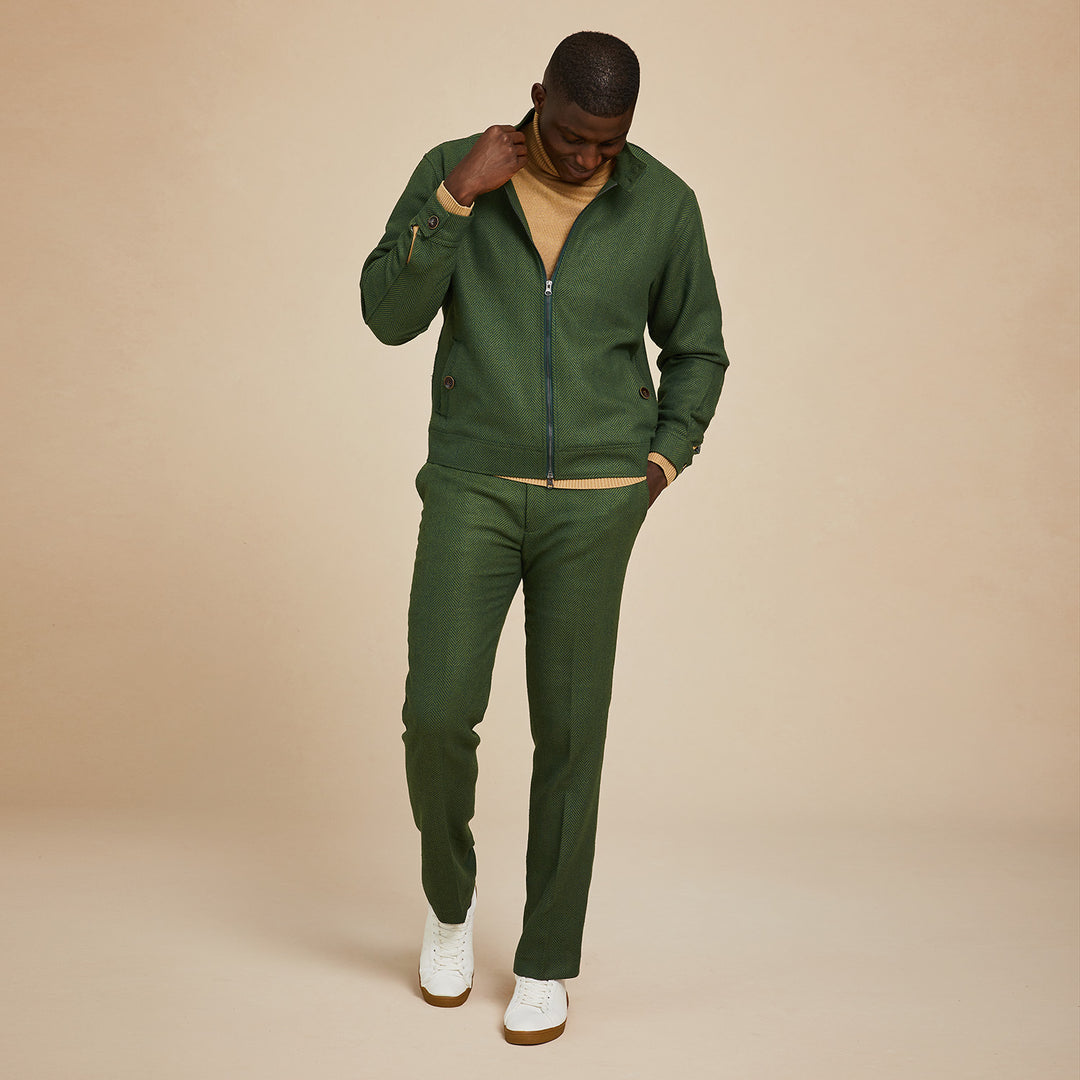 A man wears the Inserch Wool Blend Herringbone Jacket JS263-19 Olive with matching pants, a tan sweater, and white sneakers, standing against a plain beige background.