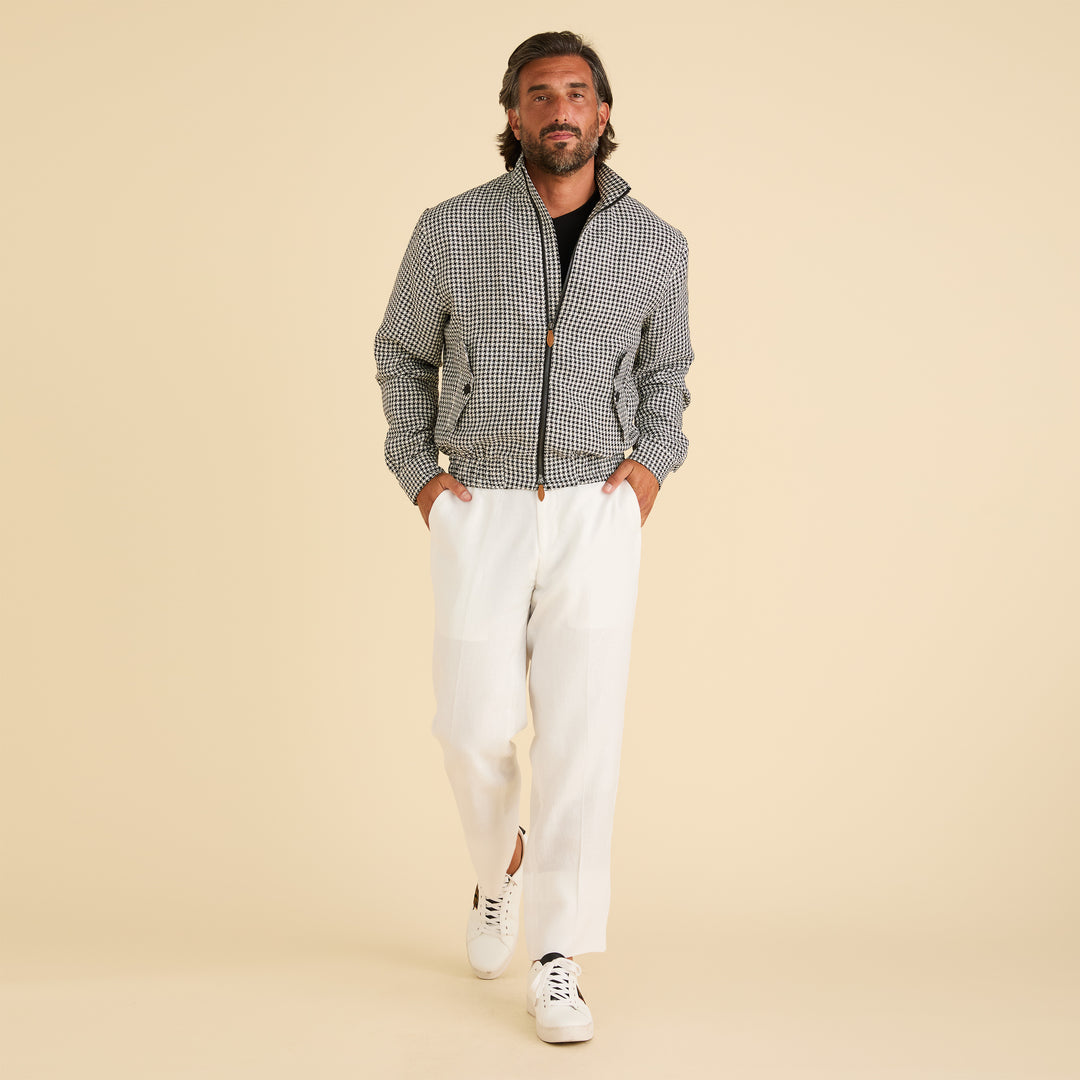 A man stands against a beige background wearing the Inserch Linen Houndstooth Jacket JS269-00041 Black & White by Inserch, paired with white pants, a black shirt, and white sneakers.
