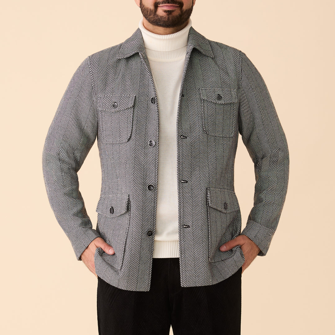 A man wears the Inserch Herringbone 4 Pocket Jacket JS273-00041 in Black/White over a white turtleneck, hands in pockets, standing against a beige background.