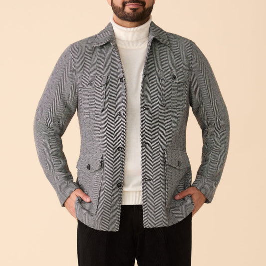 A man wears the Inserch Herringbone 4 Pocket Jacket JS273-00041 in Black/White over a white turtleneck, hands in pockets, standing against a beige background.