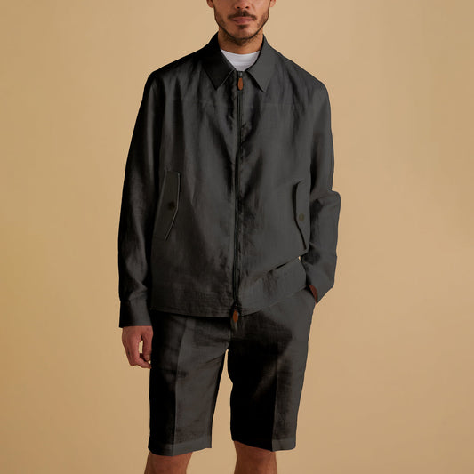A man in an Inserch Linen Harrington Jacket JS661-00001 Black, showcasing a sleek metal zipper, stands confidently against a beige background wearing shorts.