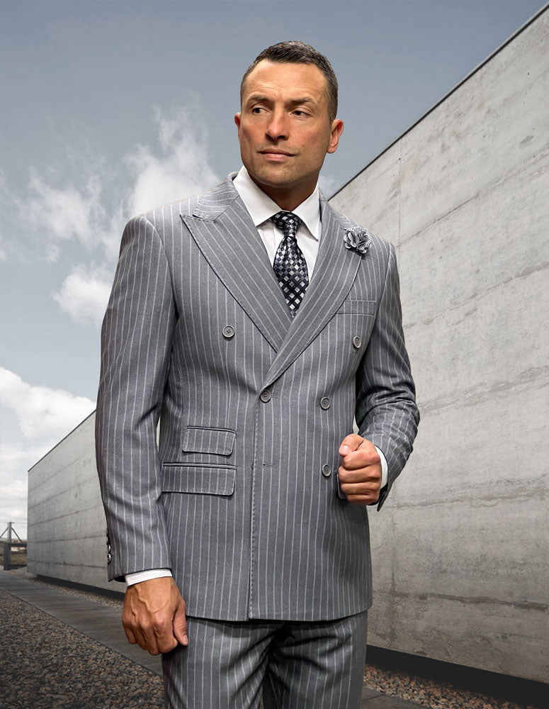 A man in the STATEMENT CLOTHING | KELLY-GREY modern-fit gray Italian wool pinstripe suit by Statement Clothing, paired with a patterned tie, stands outdoors beside a concrete wall under a cloudy sky.