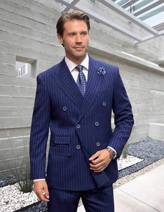 A man in the STATEMENT CLOTHING | KELLY-NAVY modern fit double-breasted Italian wool pinstripe suit by Statement Clothing stands outdoors near a modern concrete wall and minimalist landscaping, wearing a tie and watch.