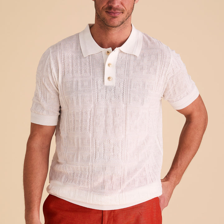 A man wears the Inserch SS Knit Polo KS001-00002 White, a short-sleeve rayon-blend polo with a collar, three buttons, and a subtle geometric knit pattern by Inserch, standing against a beige background.