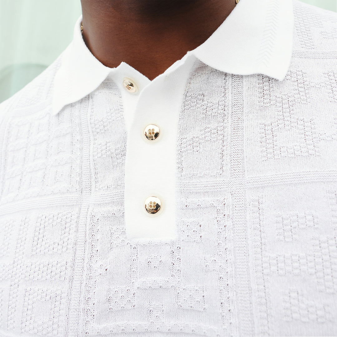 A man wears the Inserch SS Knit Polo KS001-00002 White, a short-sleeve rayon-blend polo with a collar, three buttons, and a subtle geometric knit pattern by Inserch, standing against a beige background.