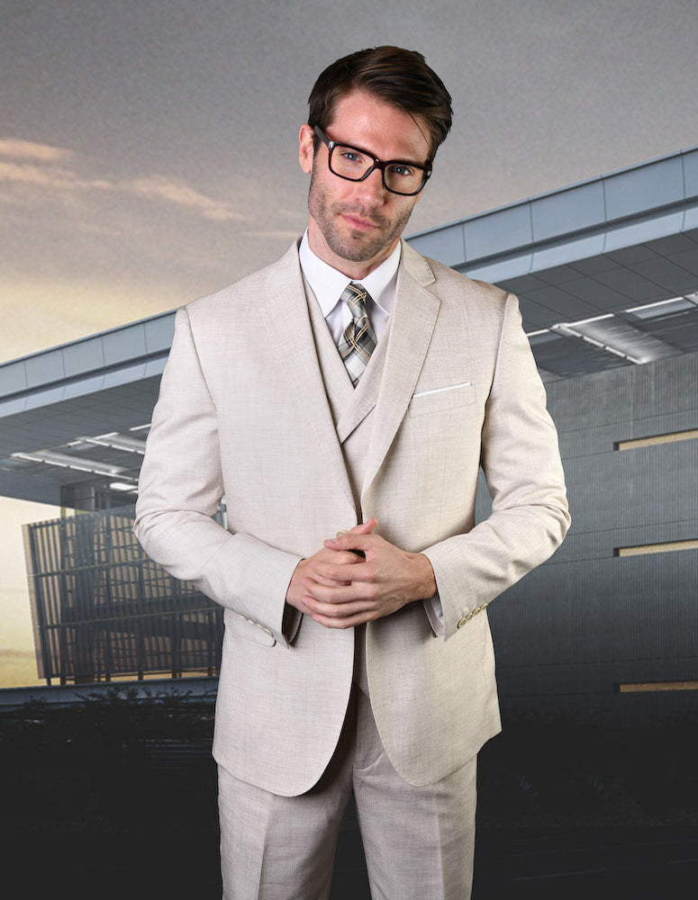 A man in a Statement Clothing LANZO-NATURAL suit and plaid tie stands before a modern building, wearing glasses and a neutral expression.