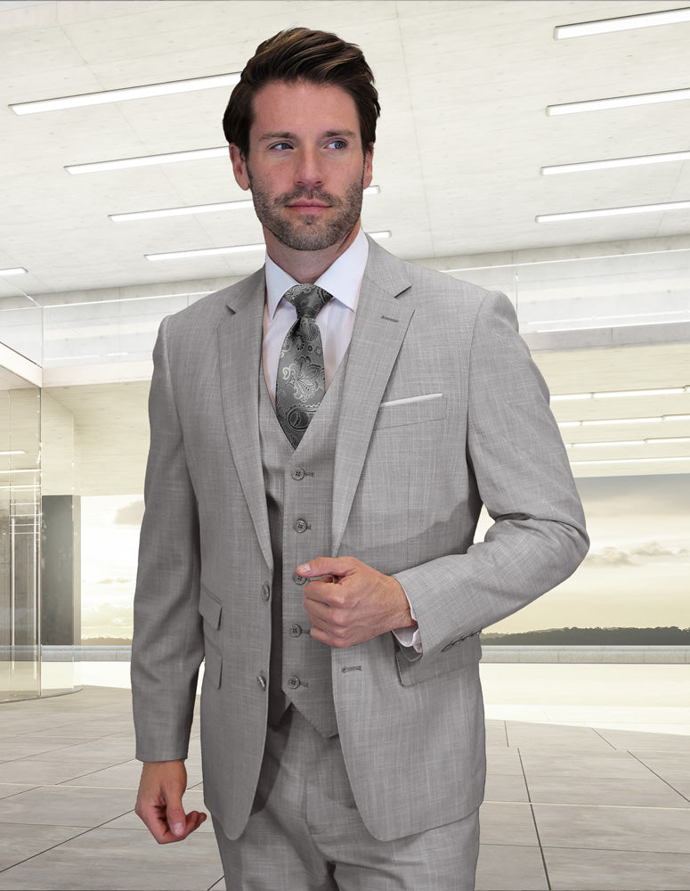 A man wears the Statement Clothing LARZO-GRAY modern fit Italian wool suit with a patterned tie, standing indoors in a bright room with large windows.