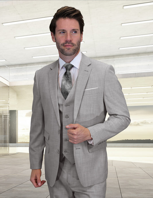 A man wears the Statement Clothing LARZO-GRAY modern fit Italian wool suit with a patterned tie, standing indoors in a bright room with large windows.