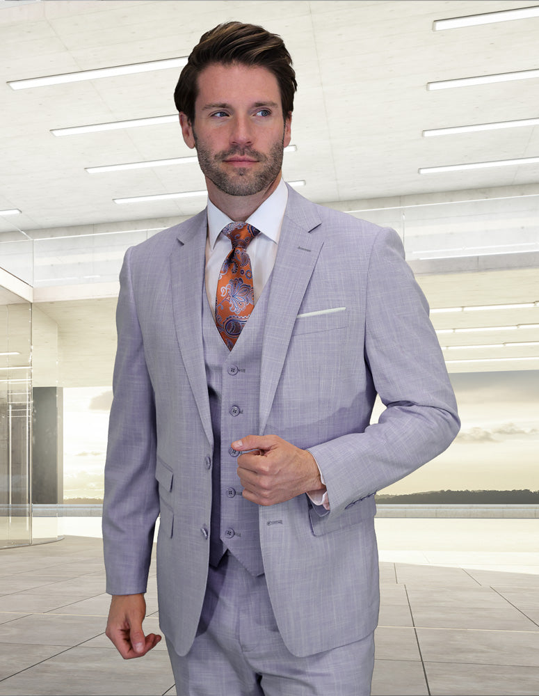A man wears the STATEMENT CLOTHING | LARZO-LAVENDER modern fit suit by Statement Clothing with a patterned tie, standing in a brightly lit, contemporary interior space.