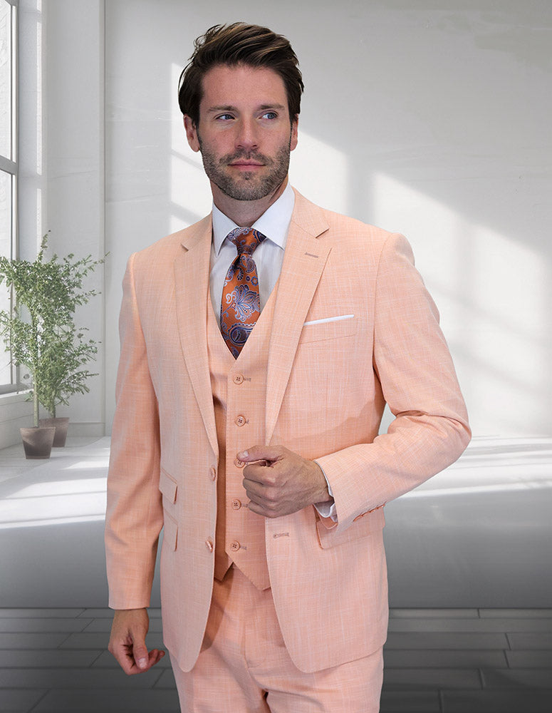 A man in the STATEMENT CLOTHING LARZO-PEACH Italian wool three-piece suit with a modern fit, patterned tie, and white shirt stands indoors by a sunlit window with a potted plant.