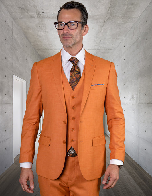 A man in the STATEMENT CLOTHING | LAZARO-RUST slim fit suit by Statement Clothing, paired with a white shirt and patterned tie, stands in a modern hallway with concrete walls.