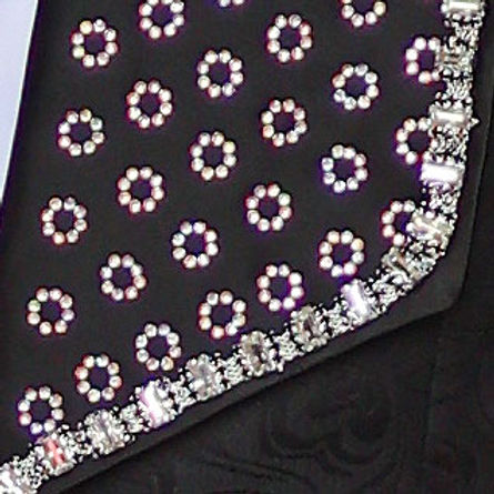 A man wears an Insomnia MANZINI LEONARDO 2-piece fancy rhinestone black tuxedo suit with a patterned lapel and bow tie, crafted from shiny fabric, standing against a textured background.