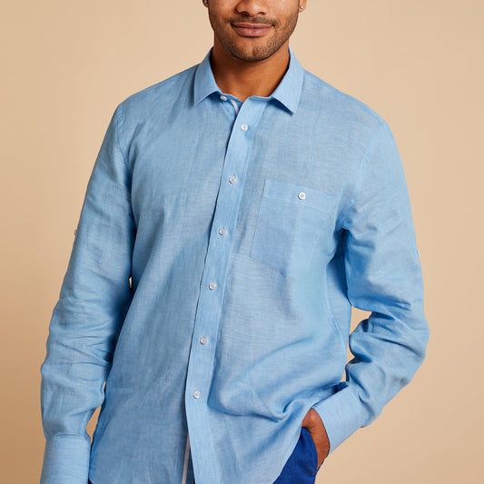 Man wearing the Inserch Linen Long-Sleeve Shirt LS29116-00154 in Lake Blue, crafted from premium European flax with a chest pocket, stands against a beige background with one hand in his pocket.