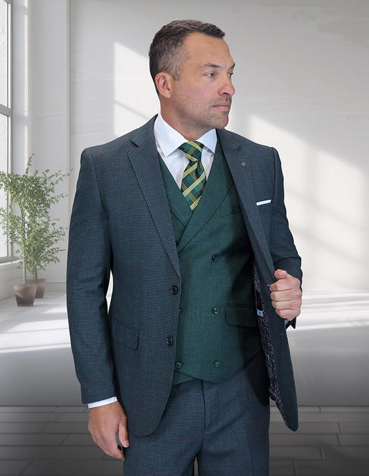 A man indoors showcases the STATEMENT CLOTHING | MARCO-2-HUNTER Italian wool suit by Statement Clothing, featuring a modern fit, green vest, and striped tie as he holds his jacket open. A potted plant is in the background.