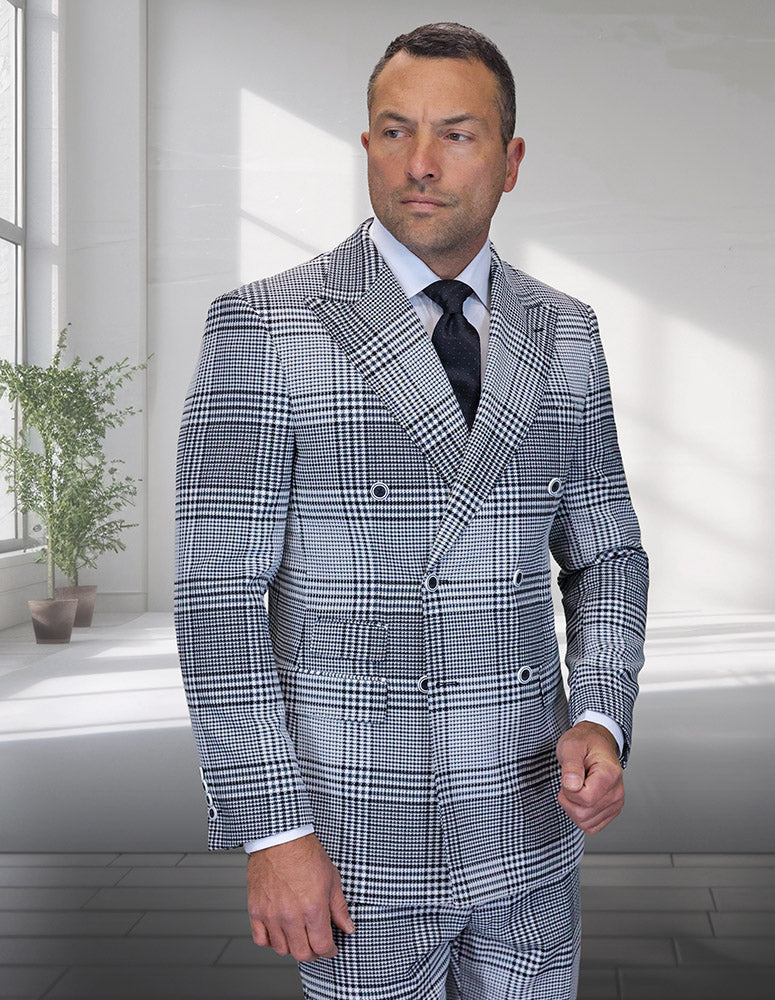 A man stands indoors near large windows in the STATEMENT CLOTHING | MILAN-NATURAL modern fit black and white plaid double-breasted Italian wool suit by Statement Clothing, with natural light and a potted plant in the background.