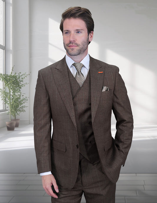 A man wearing the STATEMENT CLOTHING | MONTE-BROWN Italian wool suit by Statement Clothing, with a peak lapel, white shirt, and patterned tie, stands indoors near large windows and a potted plant.