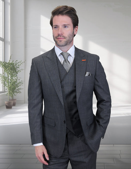 A man wears the Statement Clothing MONTE-CHARCOAL grey three-piece check suit with a modern fit, white shirt, and patterned tie, standing in a bright room with large windows and potted plants.