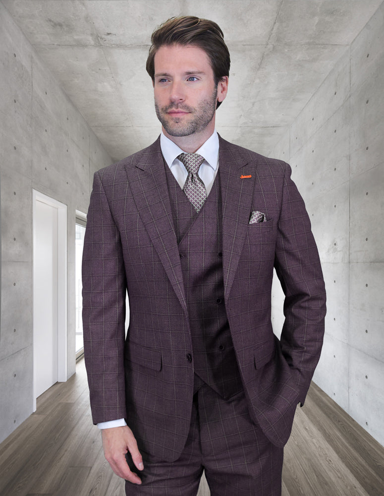 A man wearing the STATEMENT CLOTHING | MONTE-EGGPLANT suit by Statement Clothing, paired with a white shirt and patterned tie, stands in a modern hallway with concrete walls and wooden floors.