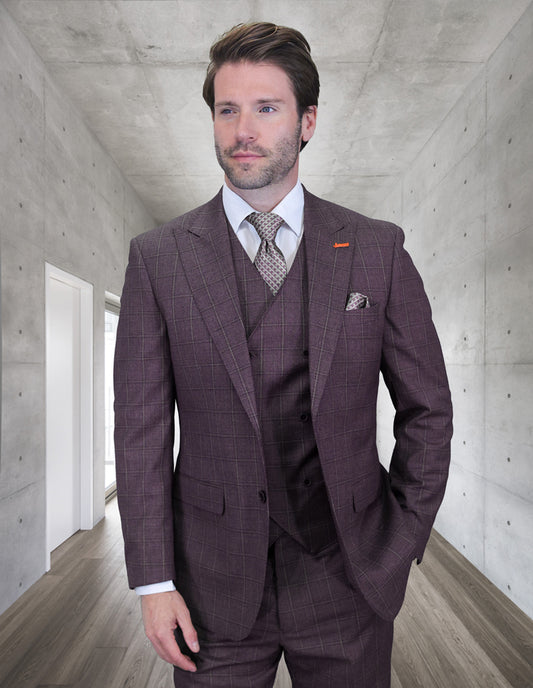 A man wearing the STATEMENT CLOTHING | MONTE-EGGPLANT suit by Statement Clothing, paired with a white shirt and patterned tie, stands in a modern hallway with concrete walls and wooden floors.