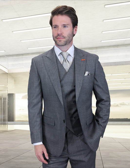 A man in the STATEMENT CLOTHING | MONTE-GRAY Italian wool suit by Statement Clothing, featuring peak lapels, a white shirt, and patterned tie, stands in a modern, brightly lit office space.