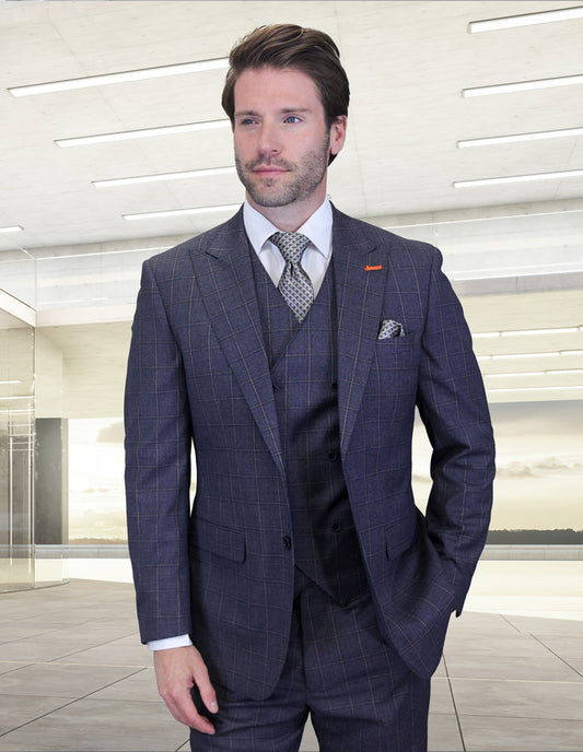 A man in the STATEMENT CLOTHING | MONTE-INDIGO suit by Statement Clothing, paired with a white shirt and patterned tie, stands indoors against a well-lit, modern backdrop with one hand in his pocket.