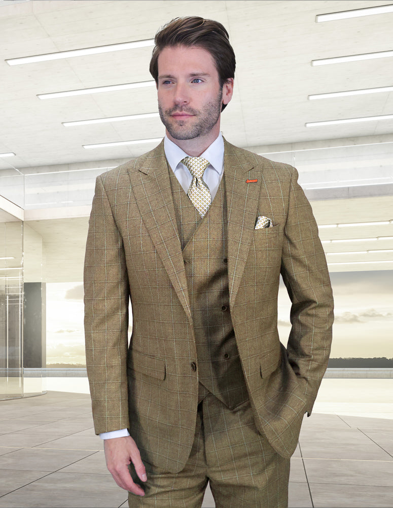 A man with light brown hair and beard wears the Statement Clothing MONTE-TAN Italian wool suit with peak lapels, paired with a white shirt and patterned tie, standing in a bright, modern indoor space.