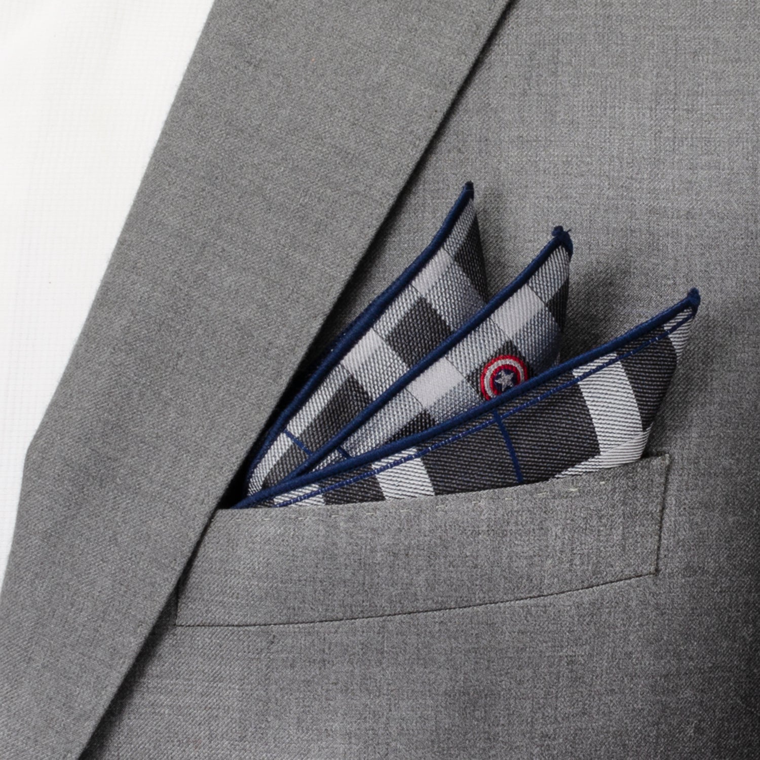 The Marvel Captain America Gray Plaid Pocket Square by Cufflinks.com features a black, white, and blue plaid design with red and white circular icons inspired by Captain America evenly spaced across the silk fabric.